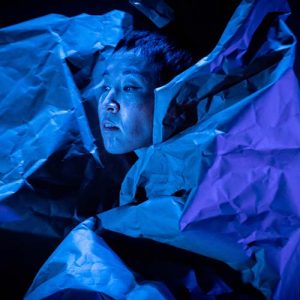 Dancer cast in blue light with crumpled paper